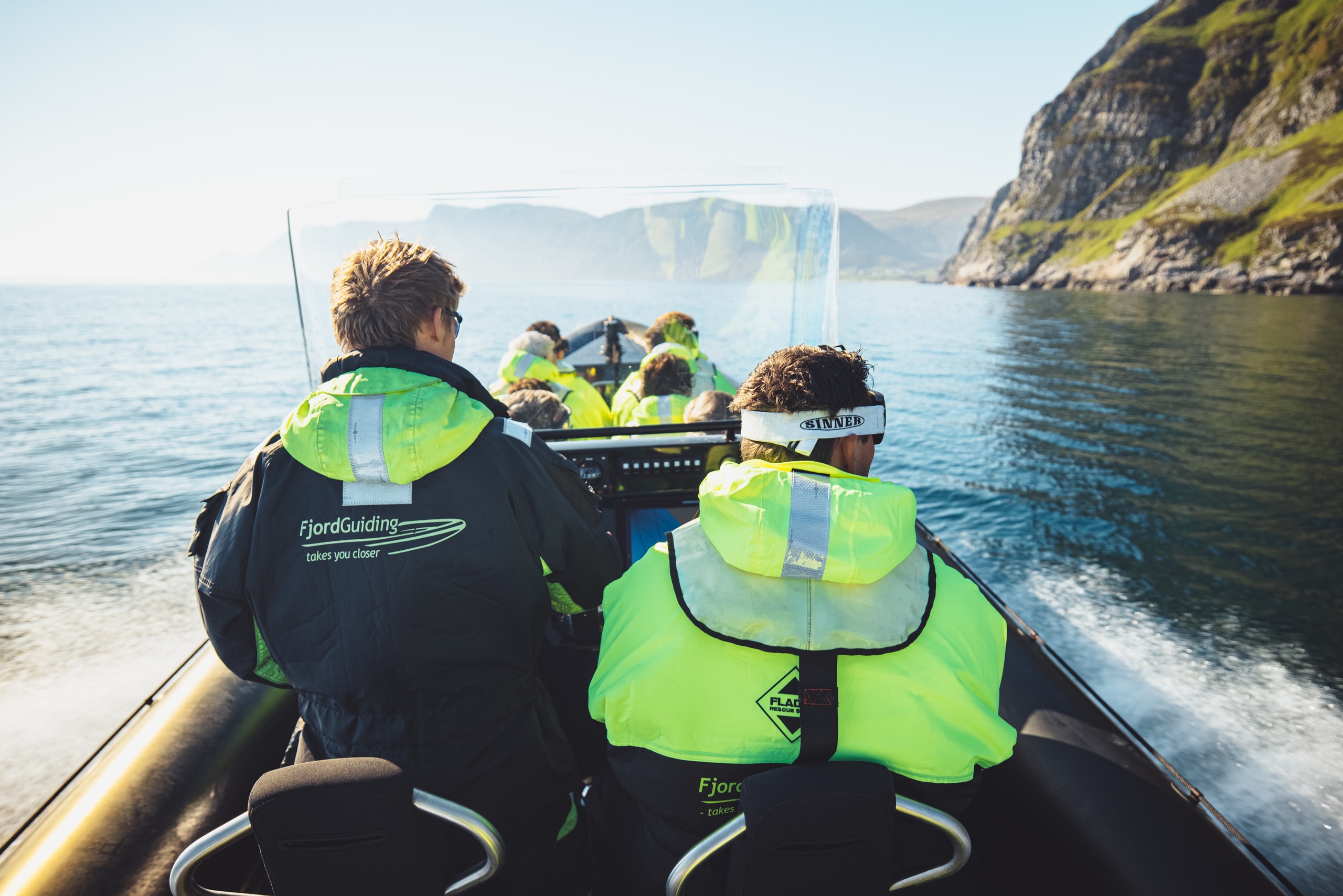 People in bright jackets on a boat near rocky cliffs on calm water.