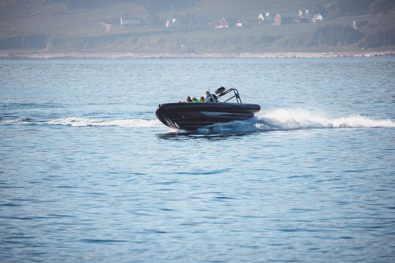 Speedboat with people cruising on calm ocean near coastline.