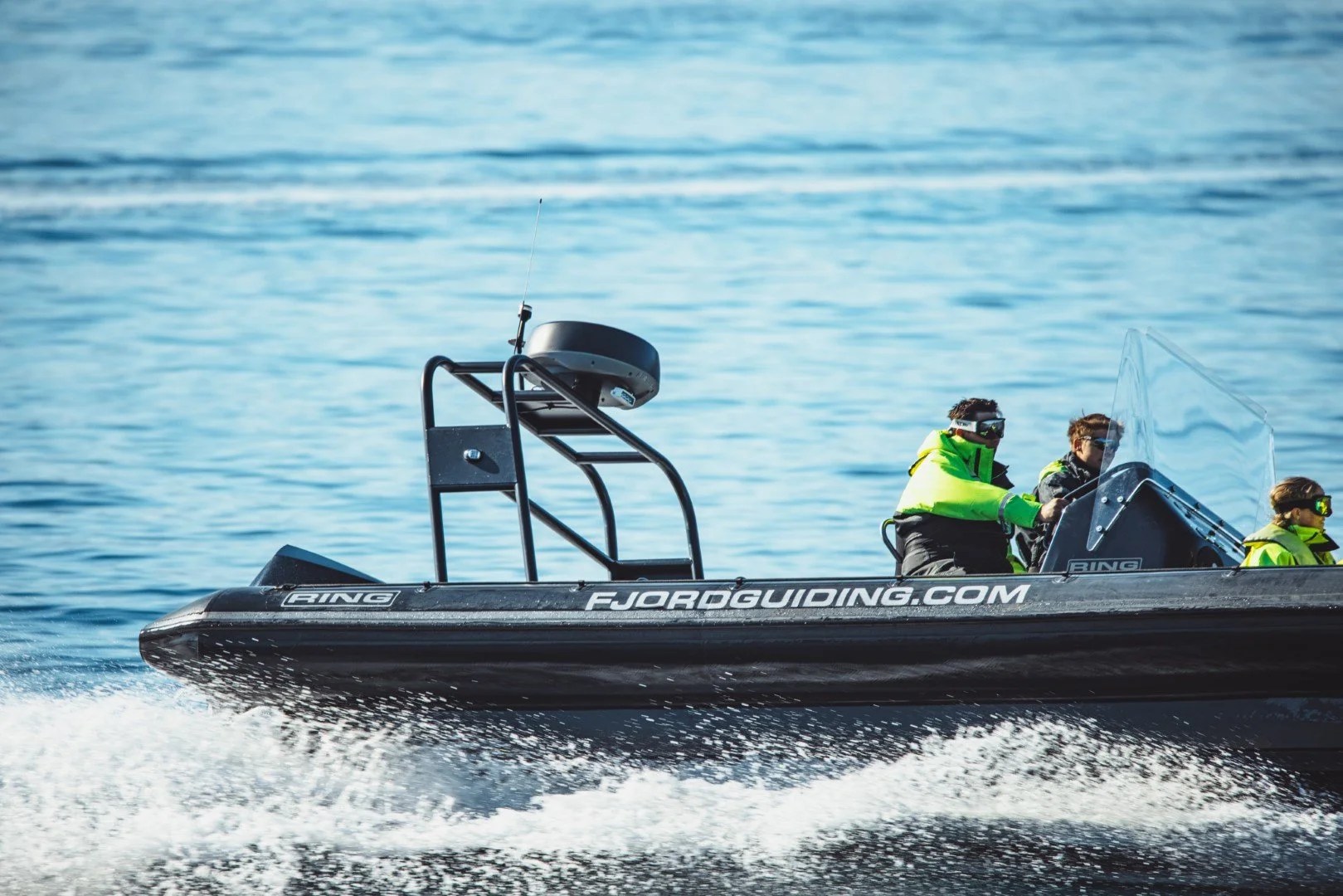 Speedboat with three people on a calm sea, wearing bright jackets.