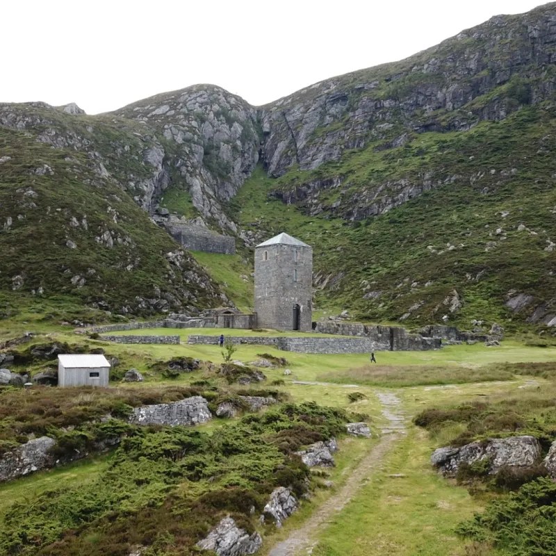 Stone tower surrounded by hills with a small building near it.