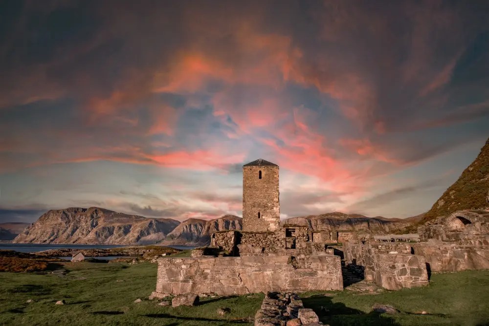Ancient stone tower with vibrant sunset sky and mountains in background.