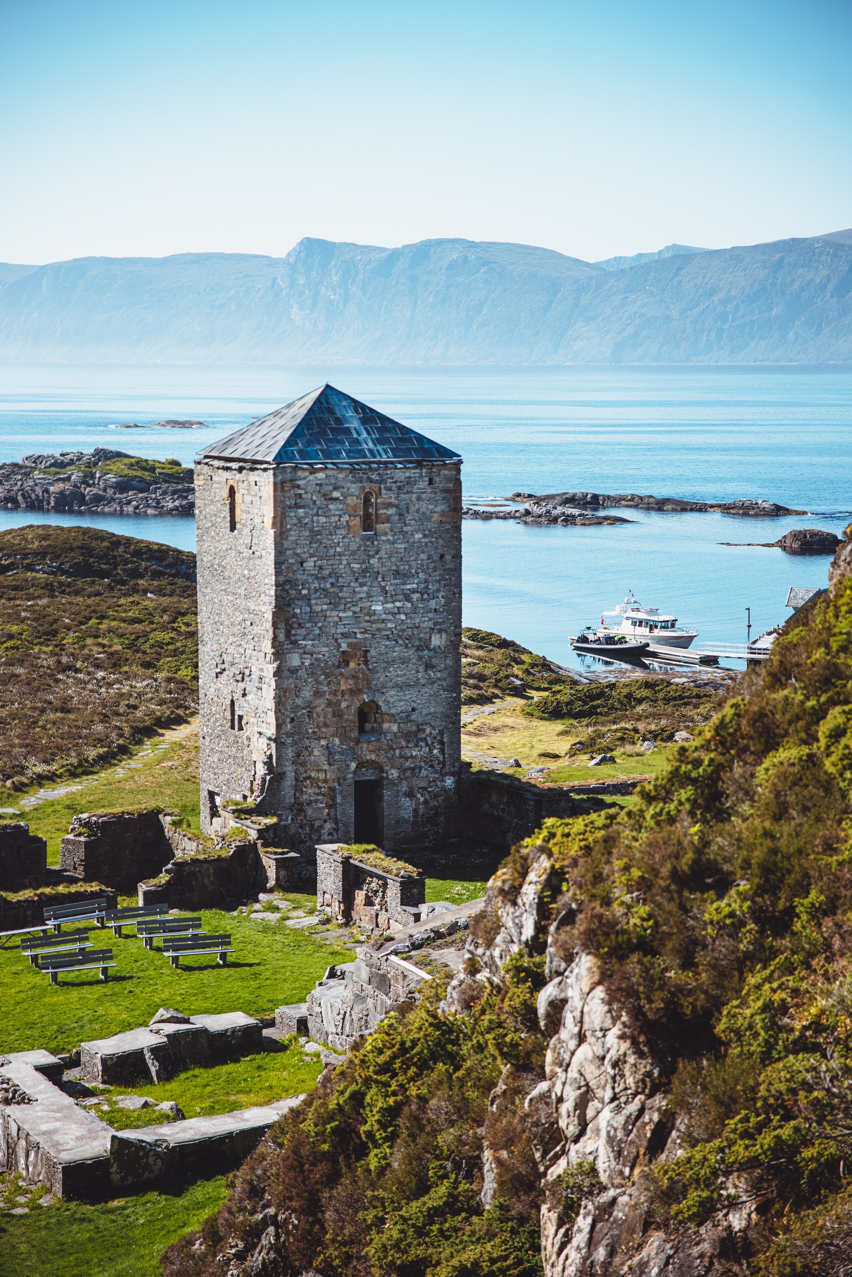 Stone tower near ruins with sea and hills in the background.
