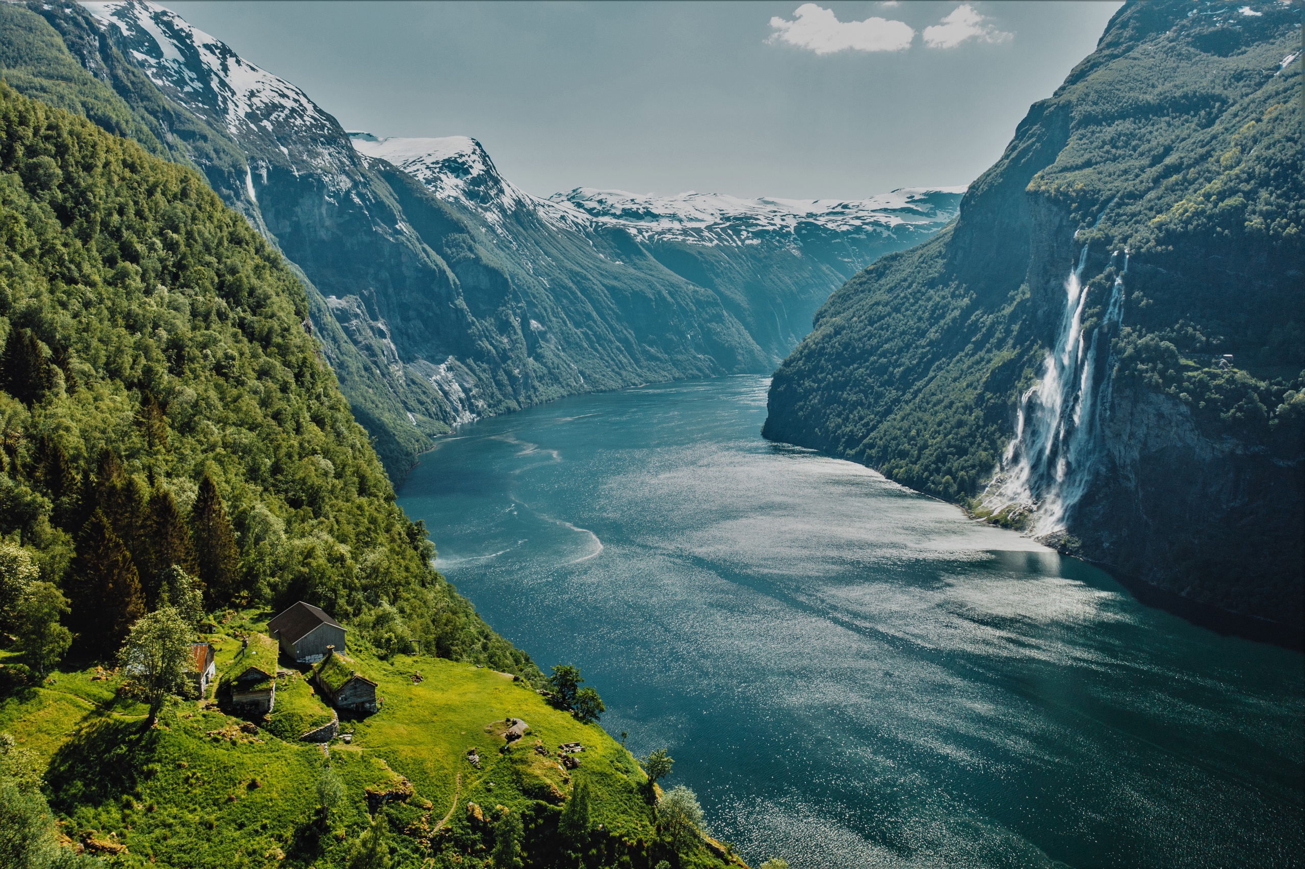 Scenic view of a fjord with mountains, a waterfall, and green hillside with houses.