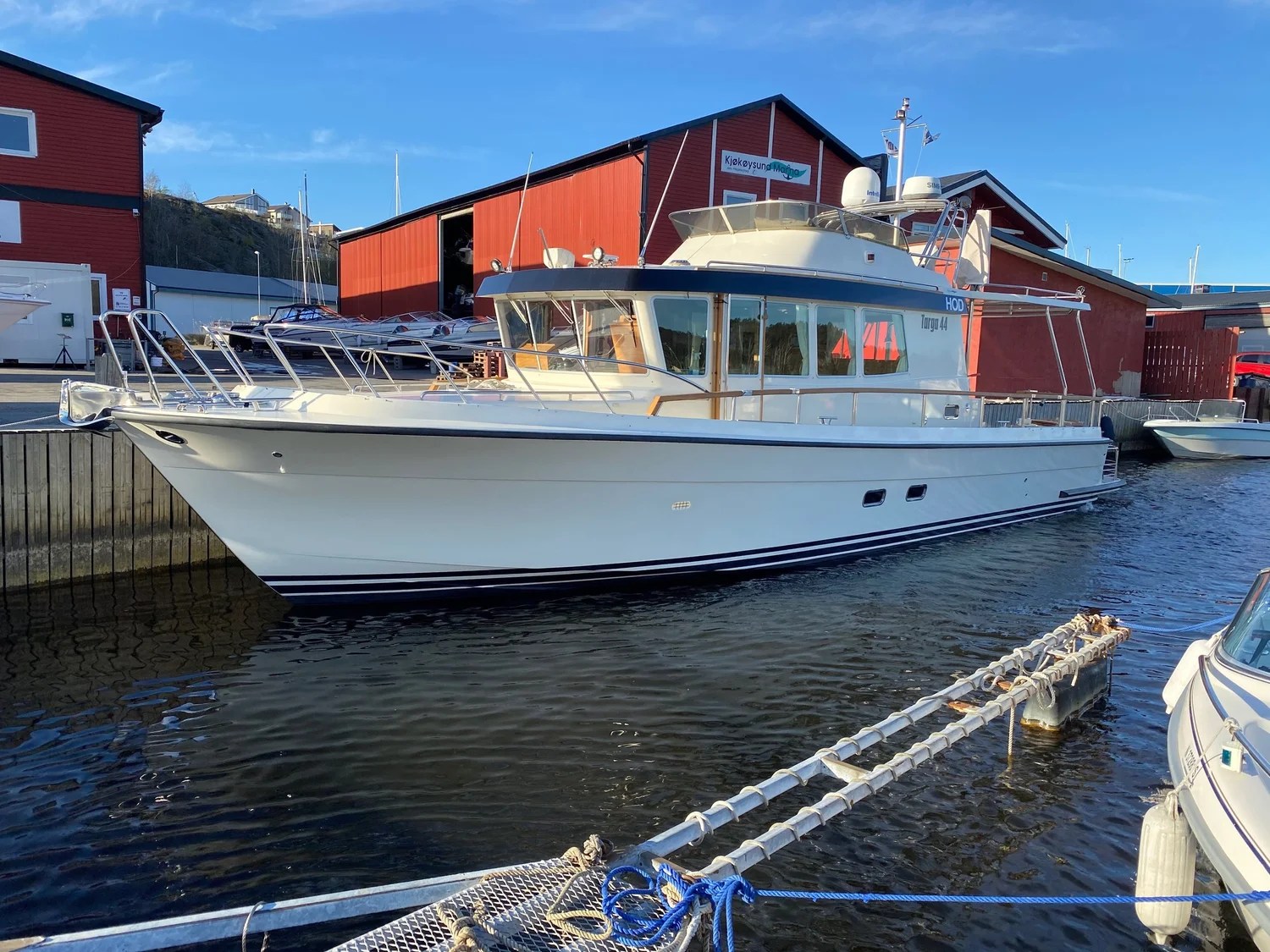 White motor yacht docked near red building.