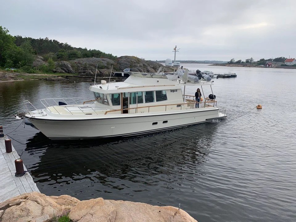 A white motorboat docked at a rocky shoreline in a calm bay.