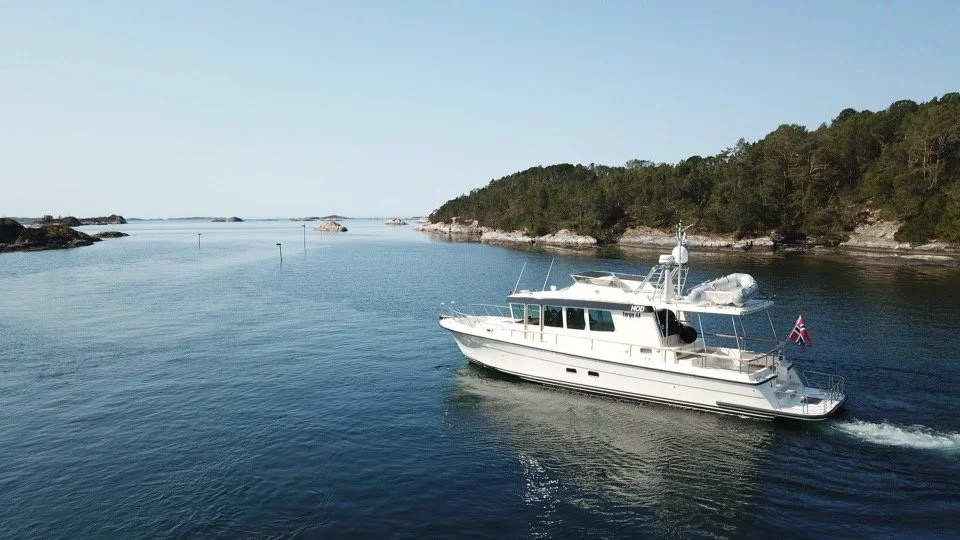 White yacht sailing in calm waters near tree-covered islands.