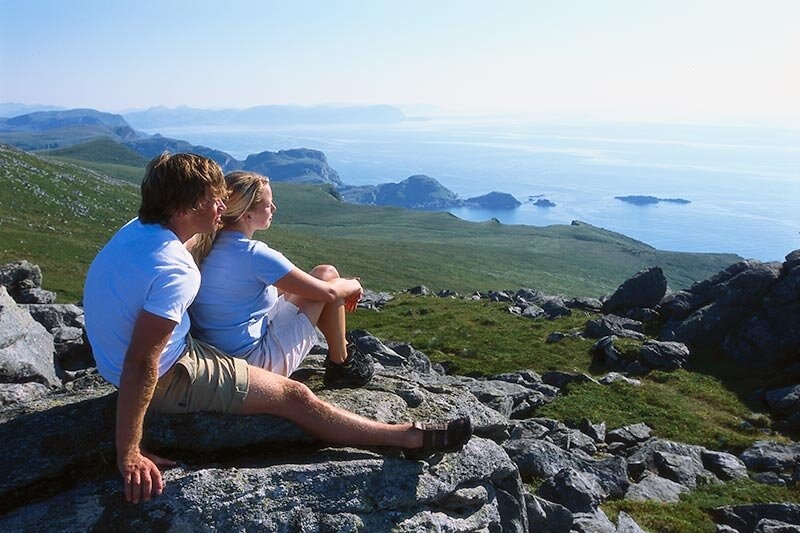 Couple sitting on rocky hill, overlooking ocean and distant islands.