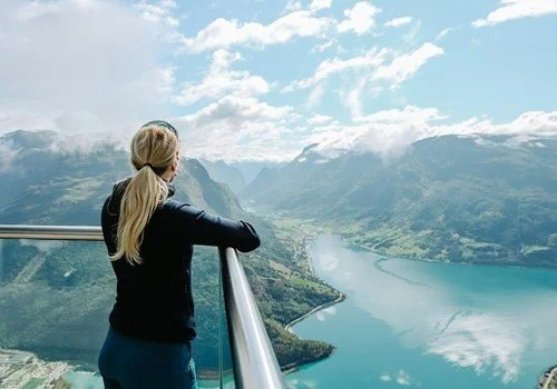 Person on balcony overlooking a fjord and mountains.