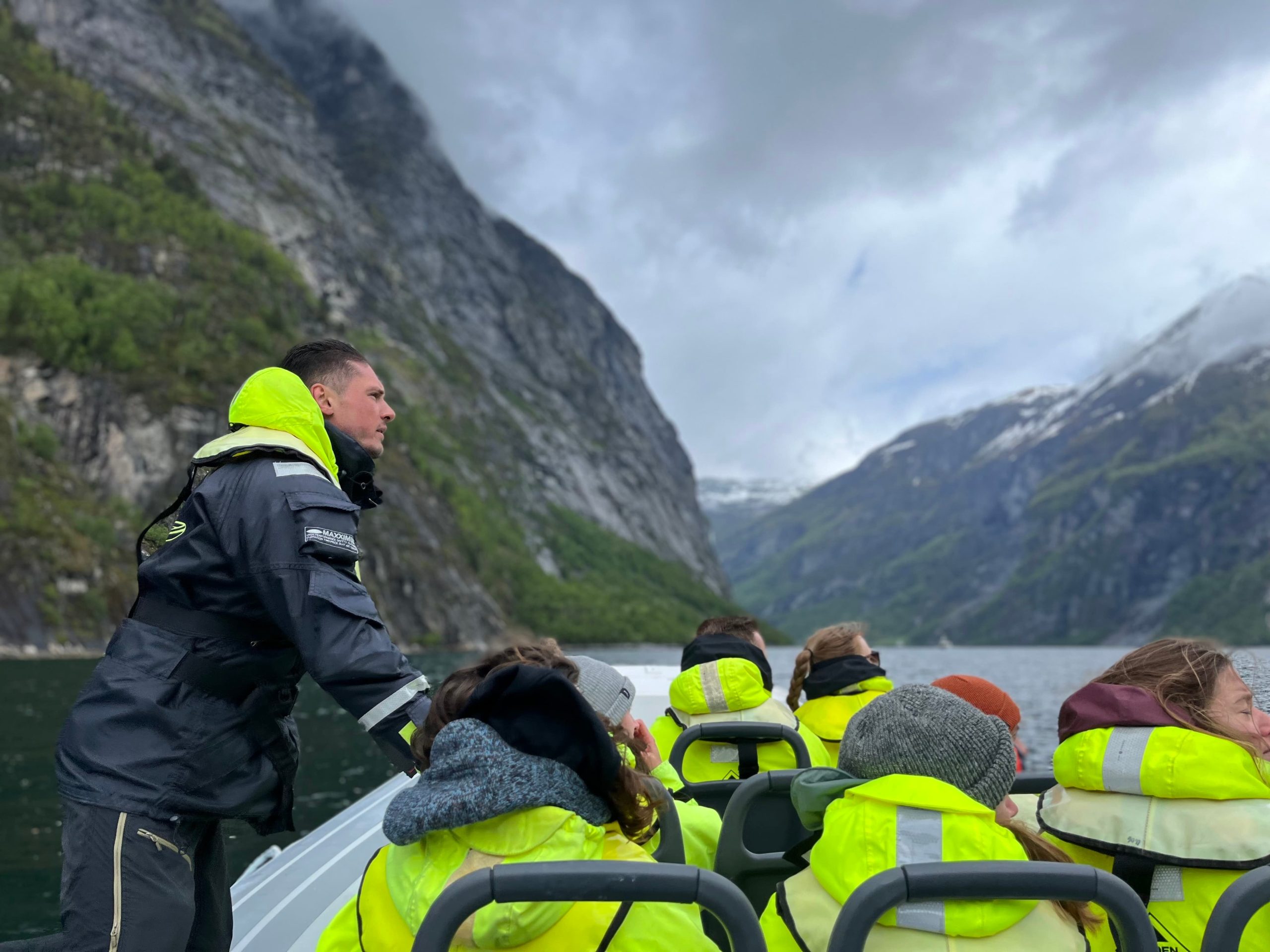 Group in yellow jackets on a boat tour through fjords with mountains and cloudy sky.