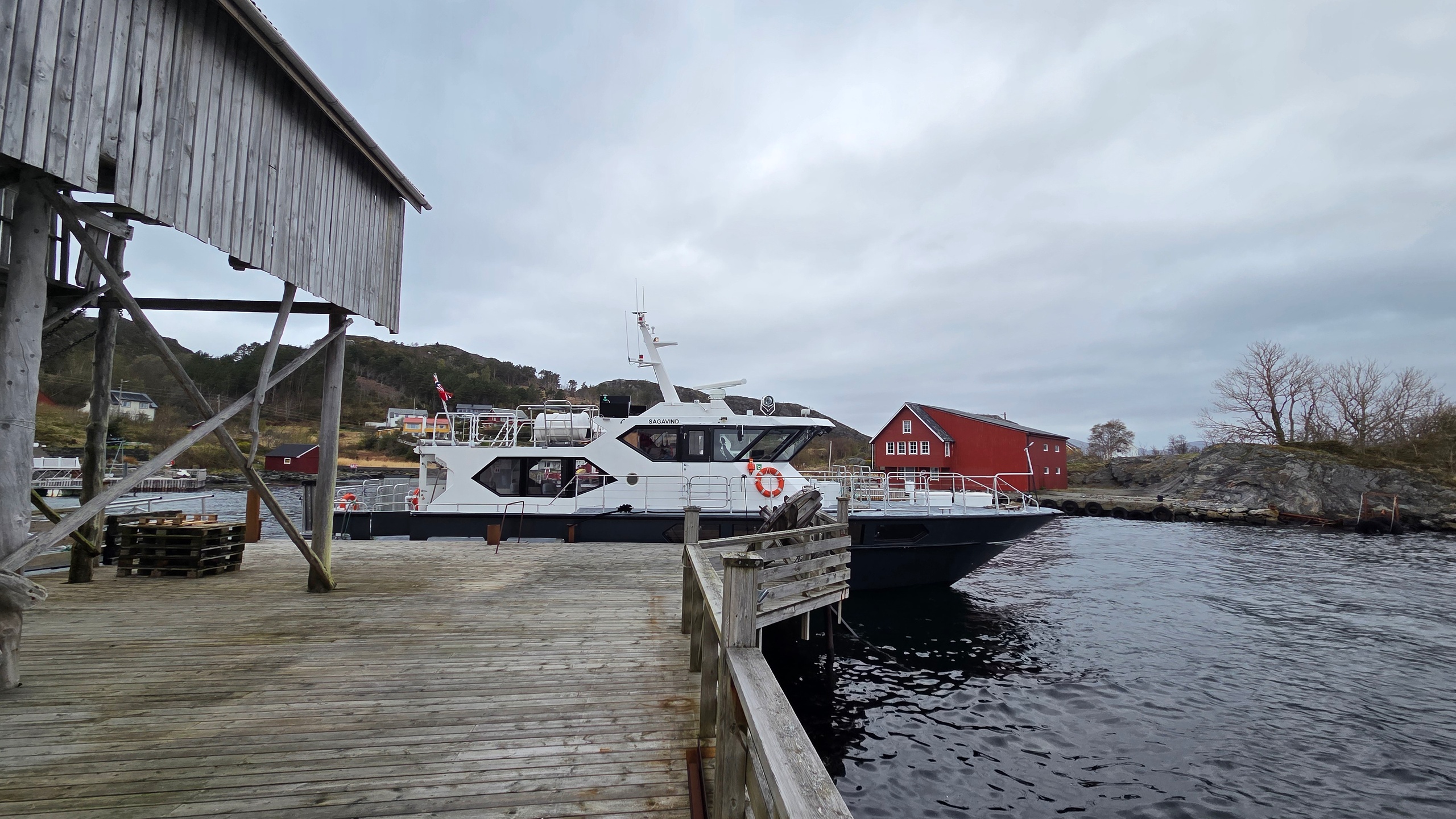 Docked boat by a wooden pier and red building on a cloudy day.