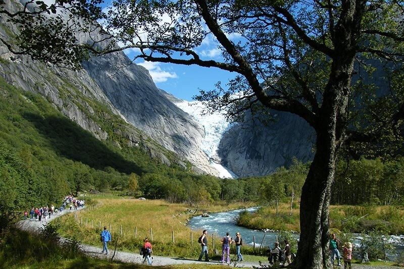 People hiking through scenic valley with a distant glacier view.