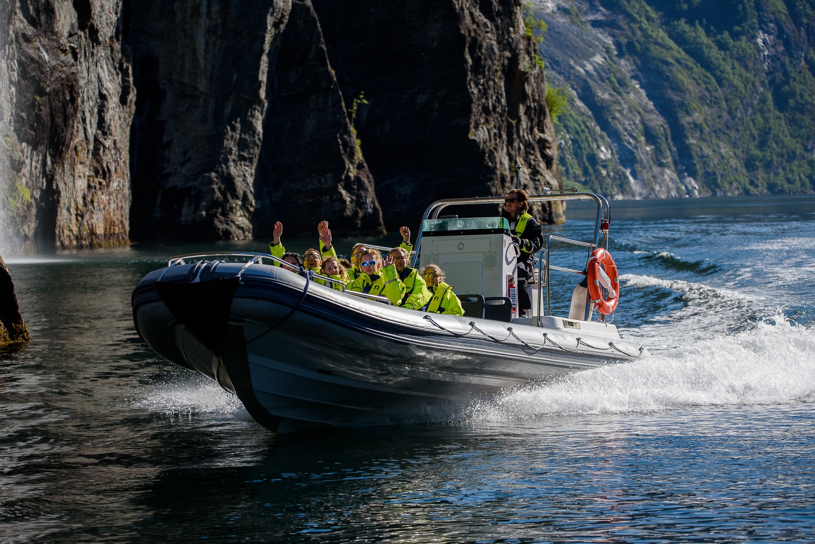 A speedboat with passengers in safety gear on a scenic waterway near cliffs.