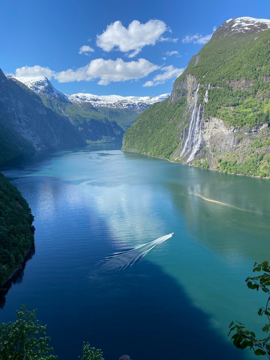 Boat sailing in a fjord with waterfalls and snow-capped mountains.