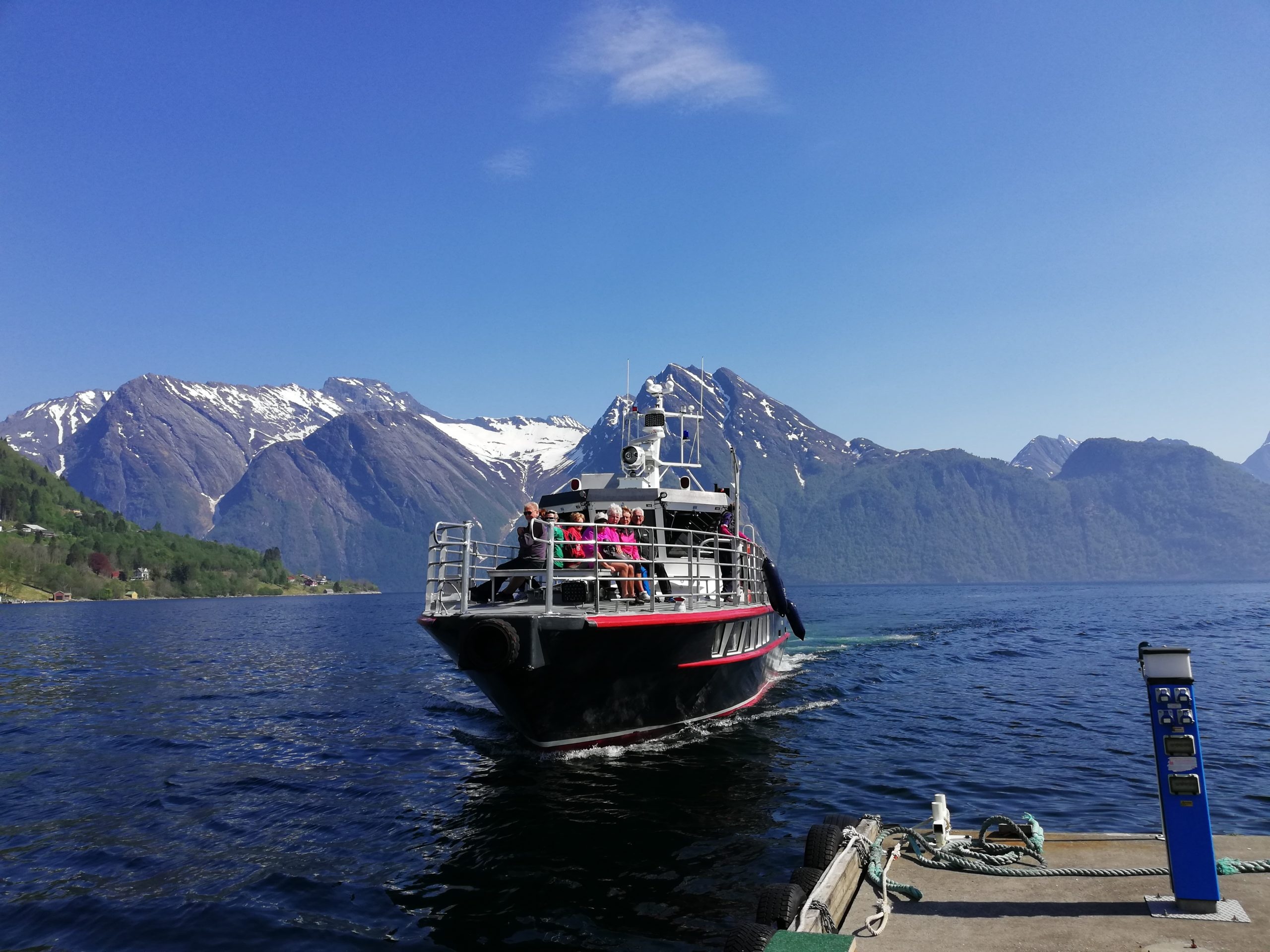 Boat approaching dock with snowy mountains in background on a clear day.