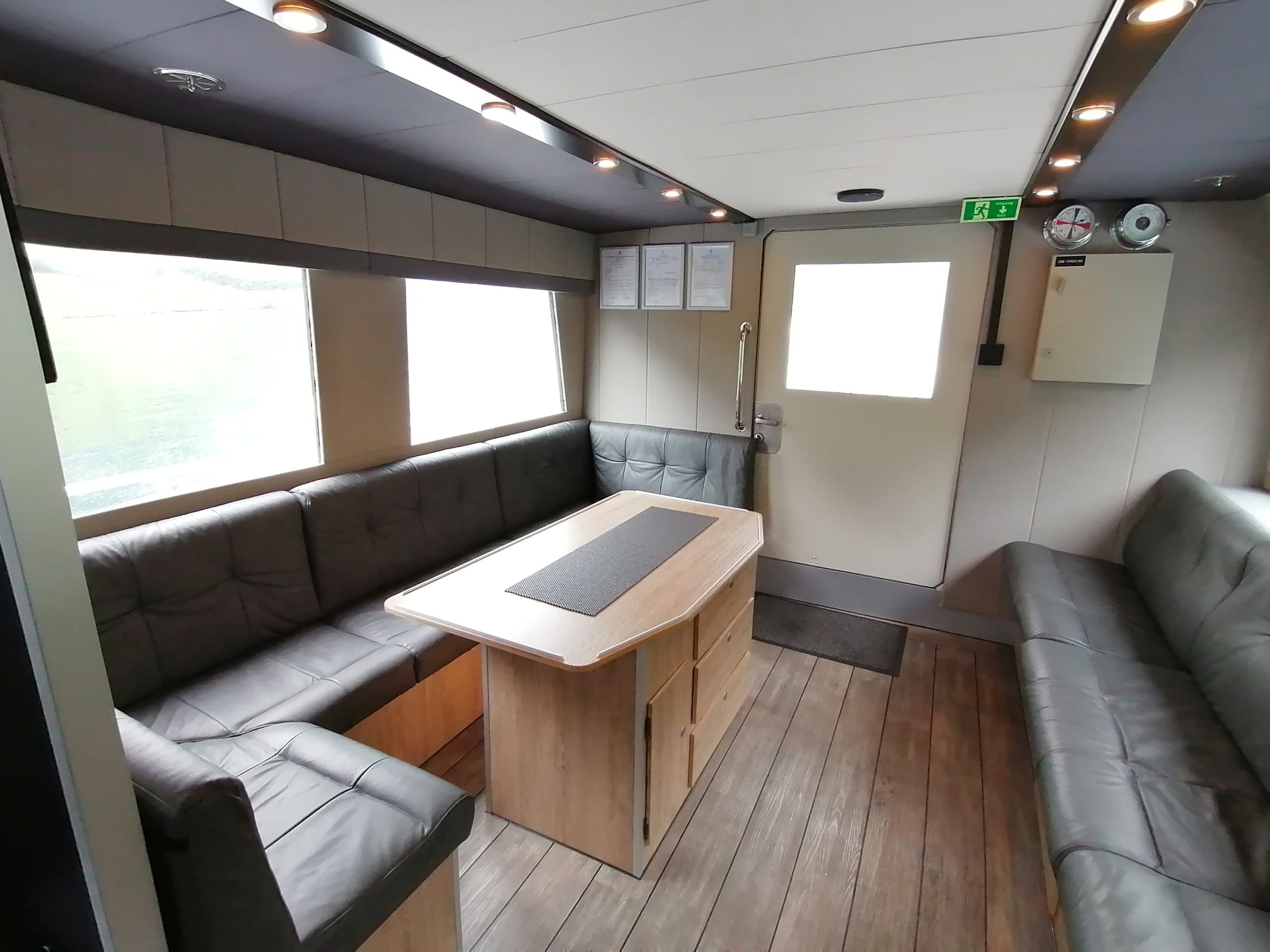 Modern boat lounge with leather seating around a wooden table and large windows.