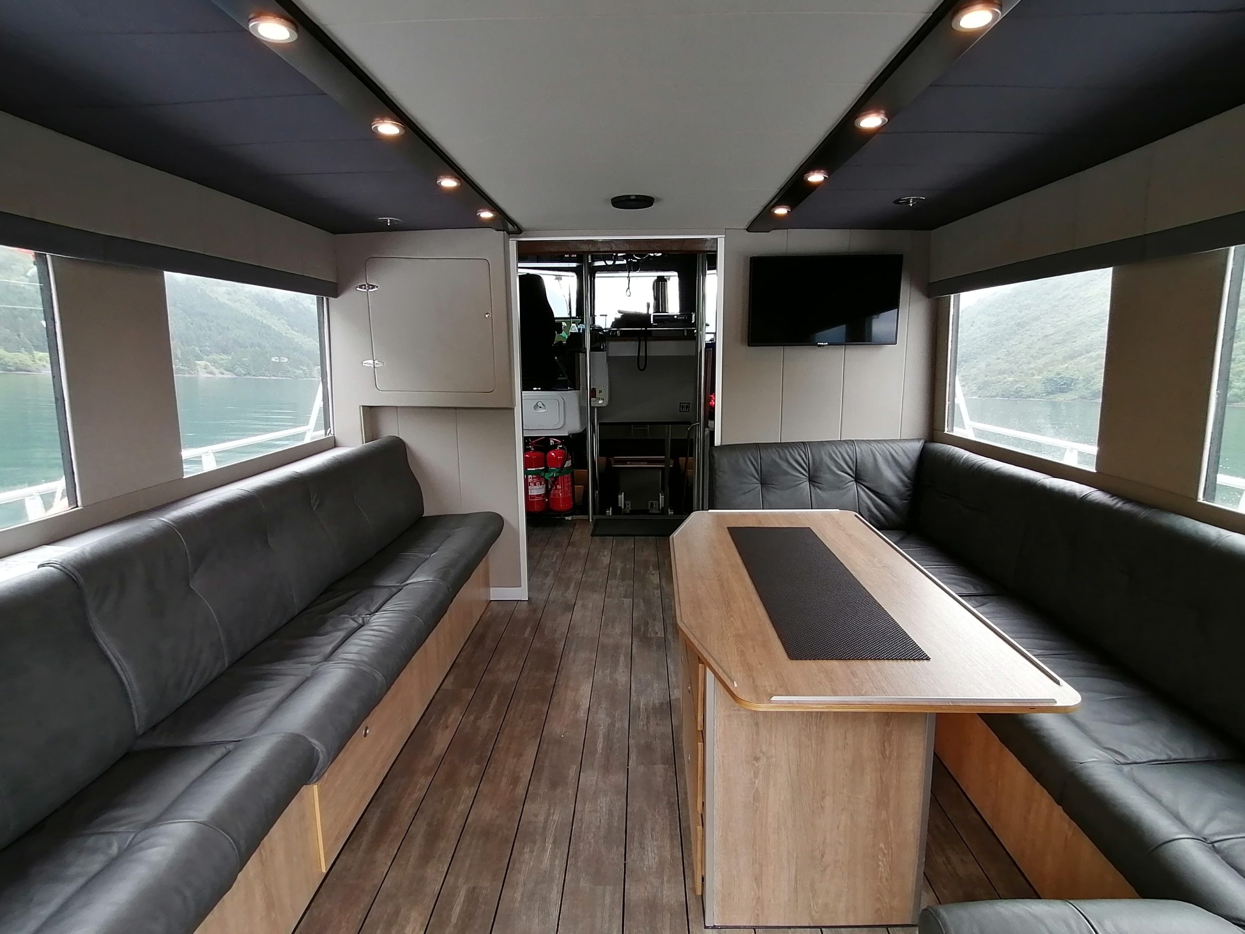 Spacious boat interior with leather seating, wood floor, and large windows.