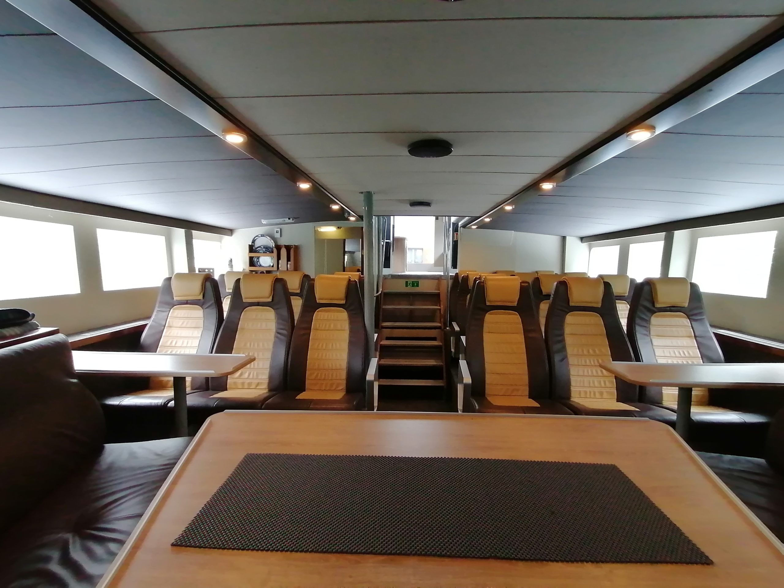 Interior of a modern ferry with rows of beige seats and tables.
