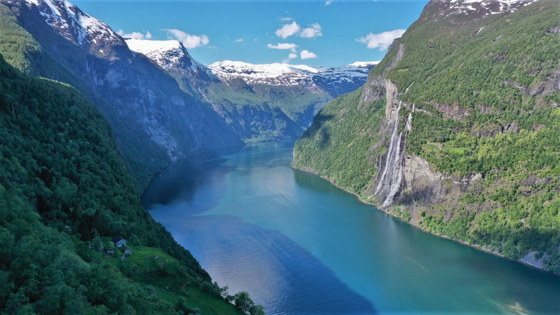 Scenic fjord with steep cliffs, waterfall, and snow-capped peaks.