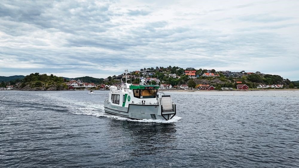 Small boat on water near a coastal village with houses and cloudy sky.