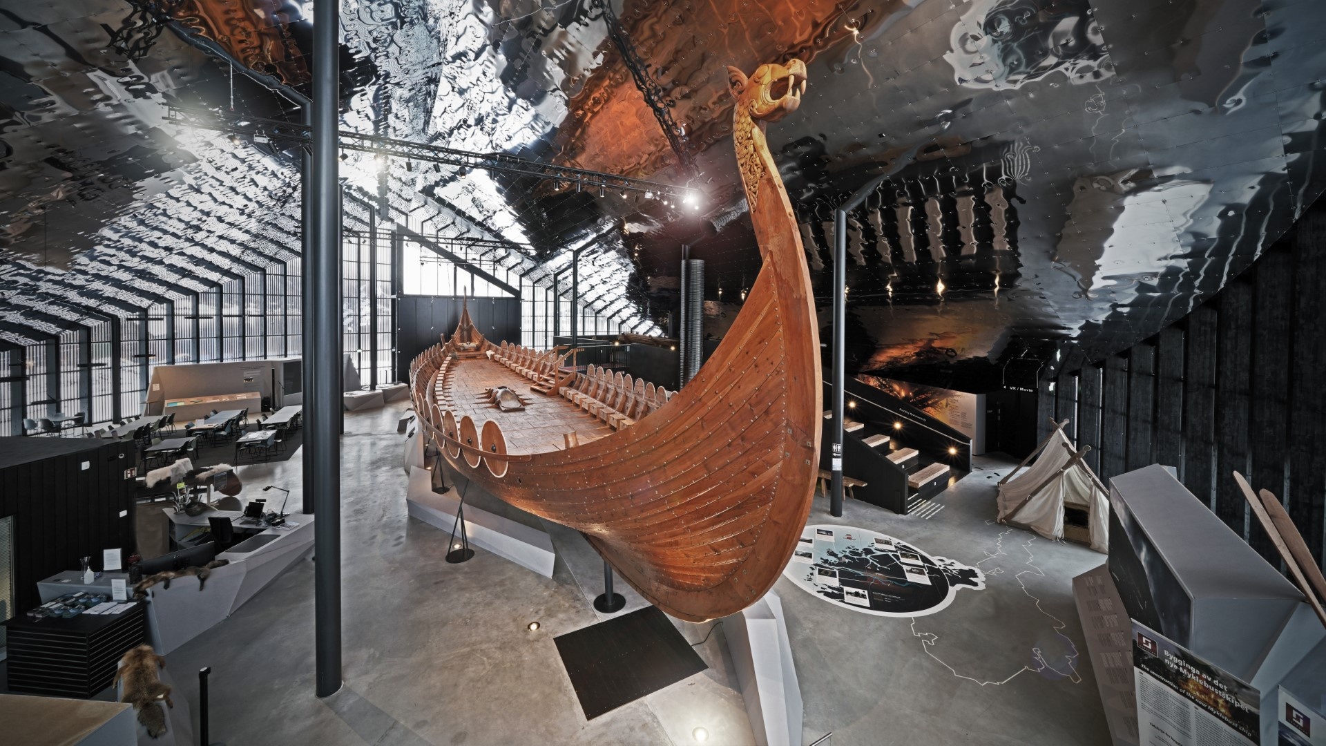 Large wooden Viking ship inside a modern museum with reflective surfaces.