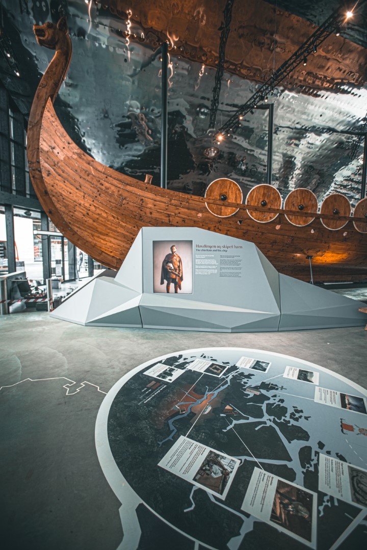 Viking ship display inside a museum with informational panels and a reflective ceiling.