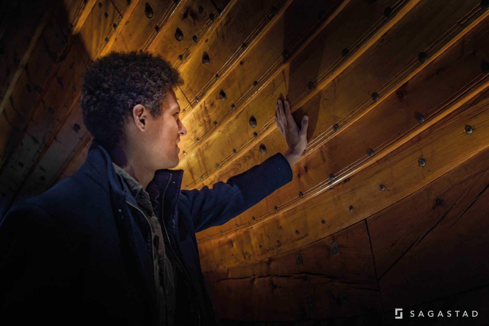 Person touching a wooden ship's interior hull with curiosity.
