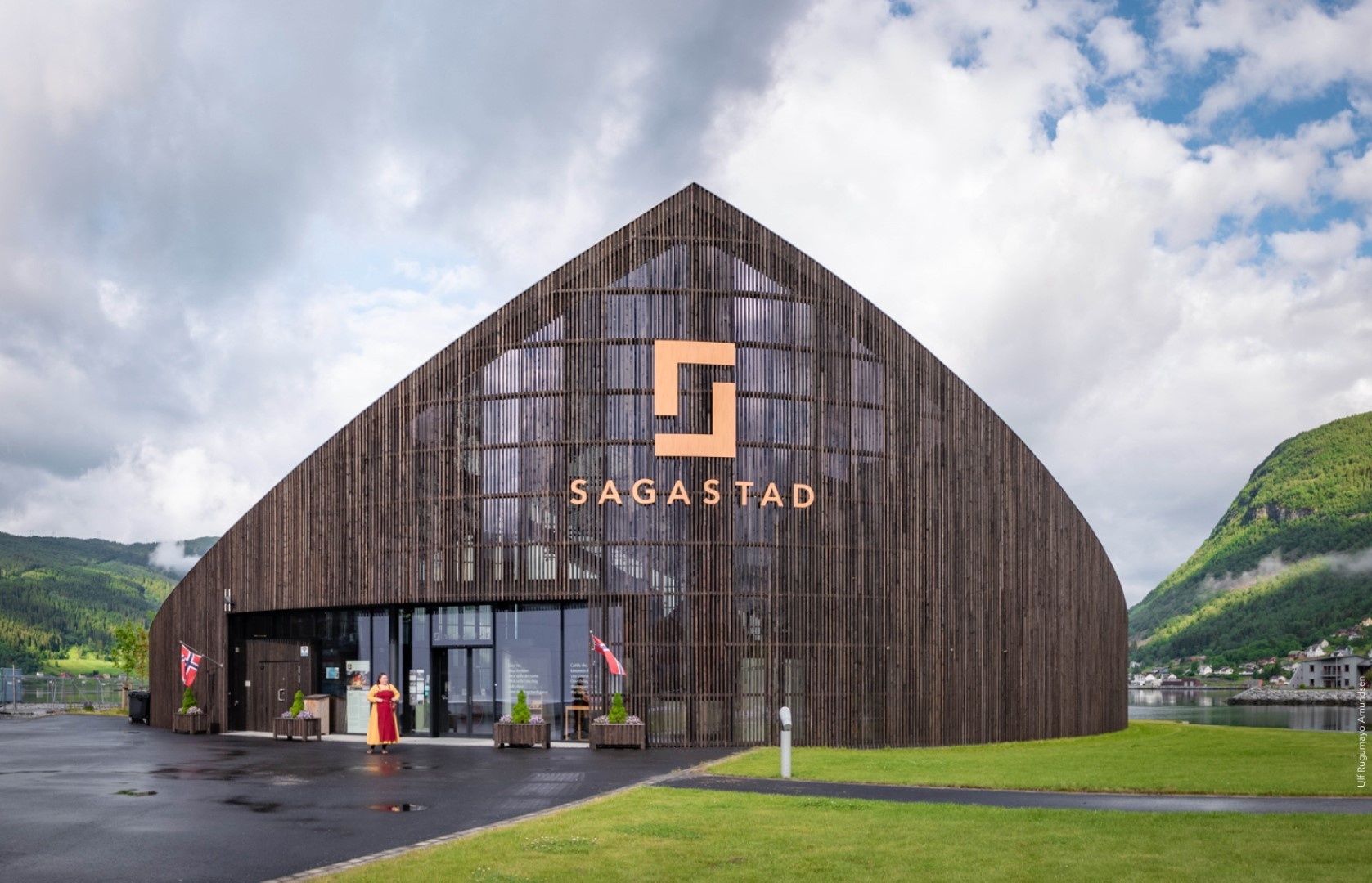 Wooden building with 'Sagastad' sign, against a backdrop of mountains and cloudy sky.
