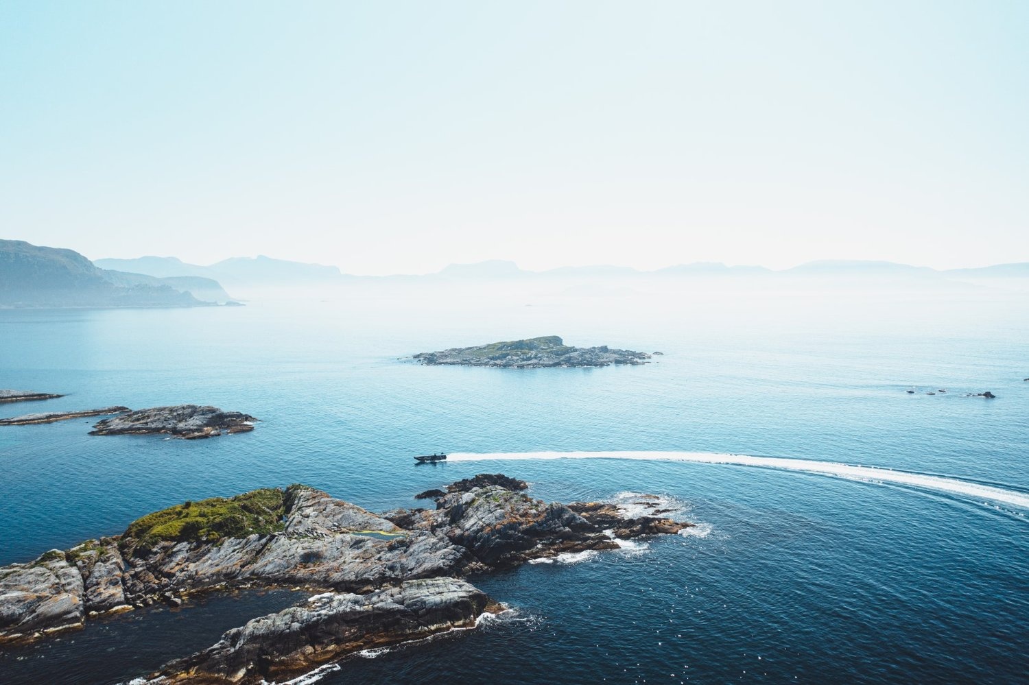 Aerial view of a speedboat leaving a wake near rocky islands in a vast blue sea.