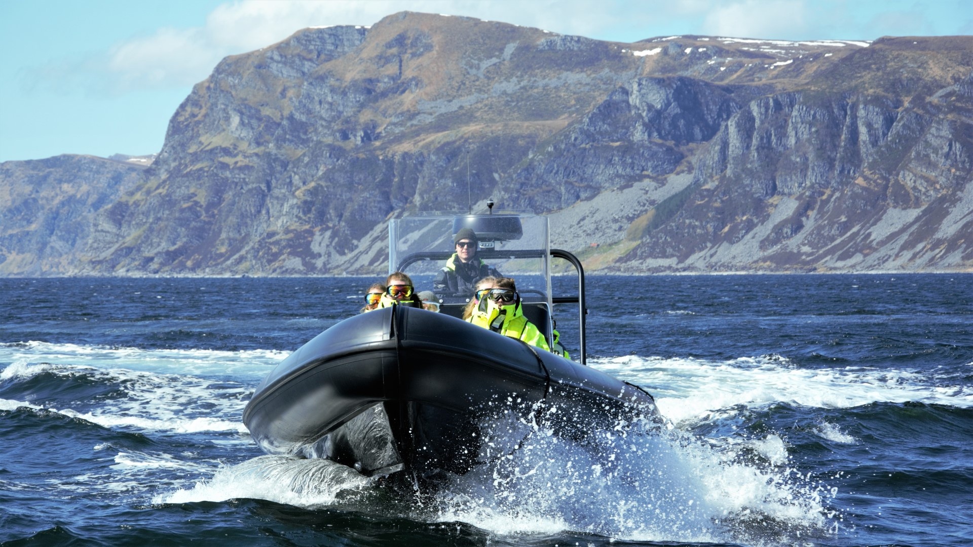 Boat with people on ocean, mountainous coast in background.