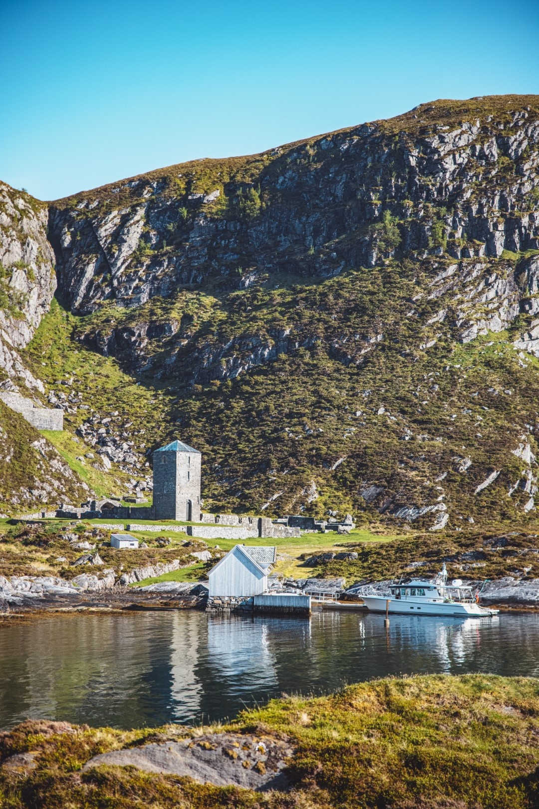 Scenic view of a stone tower by a rocky hillside with boats on a calm body of water.
