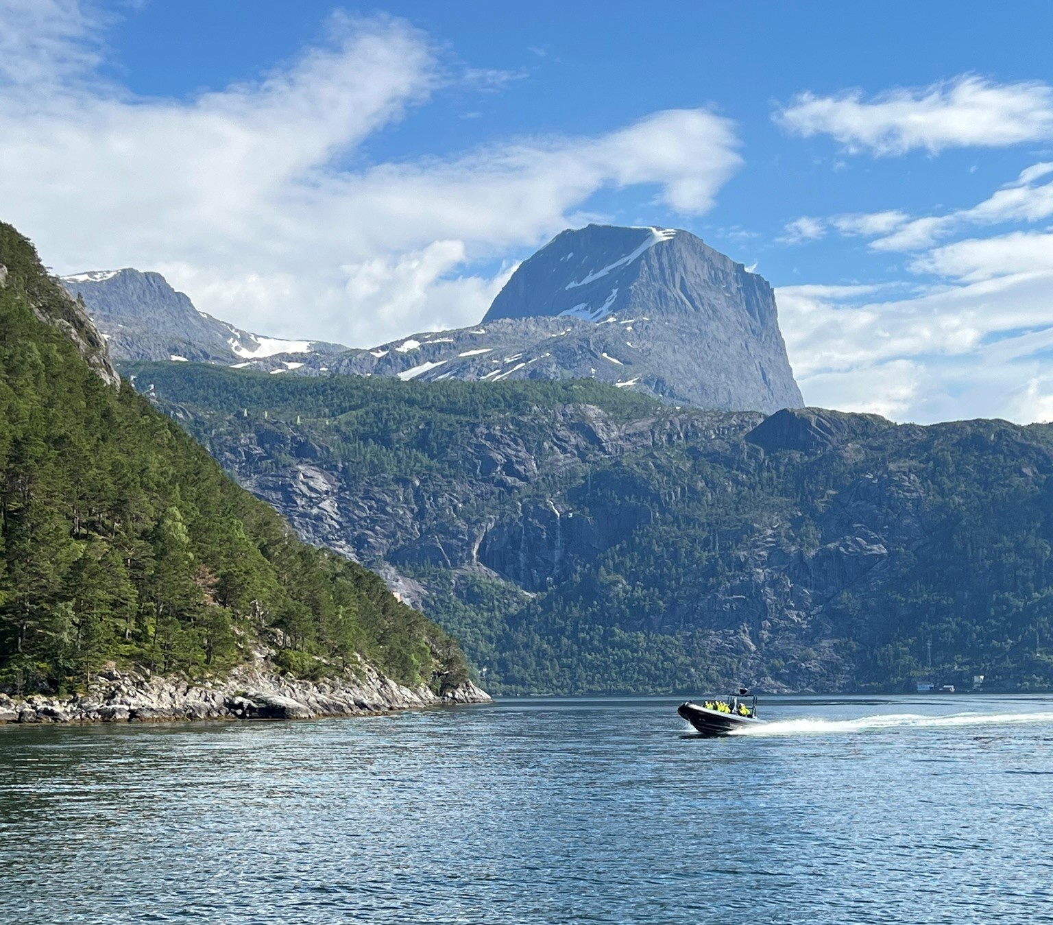 Motorboat on fjord with green mountains and blue sky.