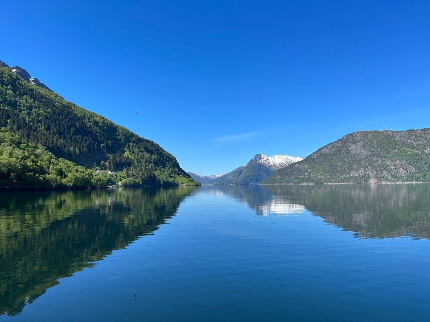 Calm lake reflecting mountains and blue sky with a few clouds.
