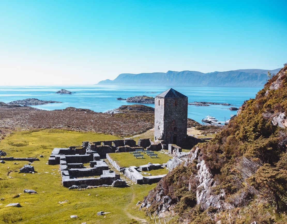 Old stone ruins by the sea with a tower and distant hills.