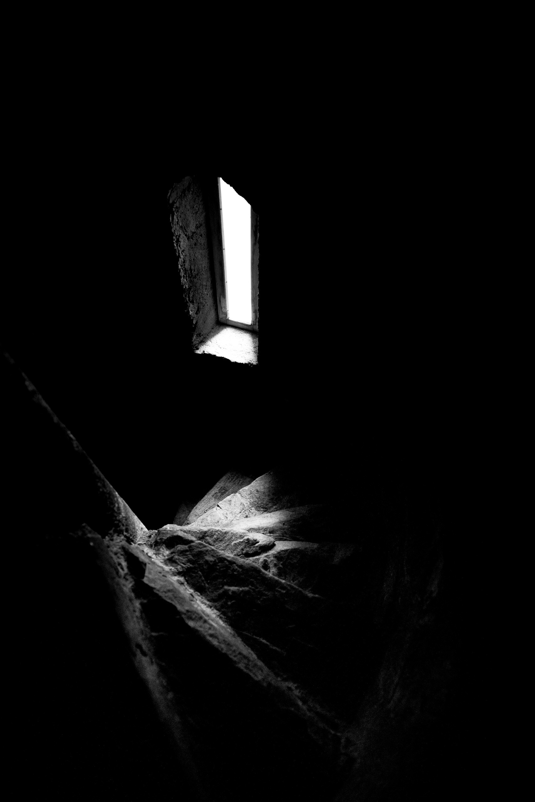 Dark spiral staircase with a small window above.
