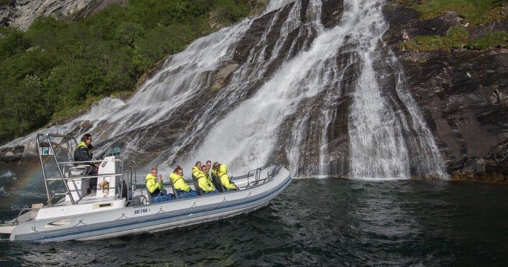 Tourists in yellow jackets on a boat near a waterfall and rocky landscape.