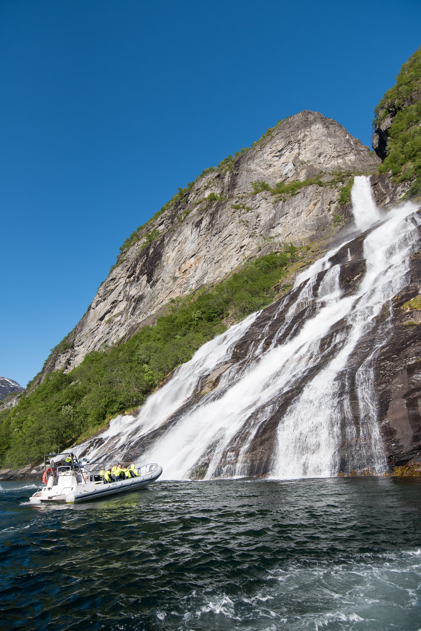 Boat near a large waterfall cascading down a rocky cliff.