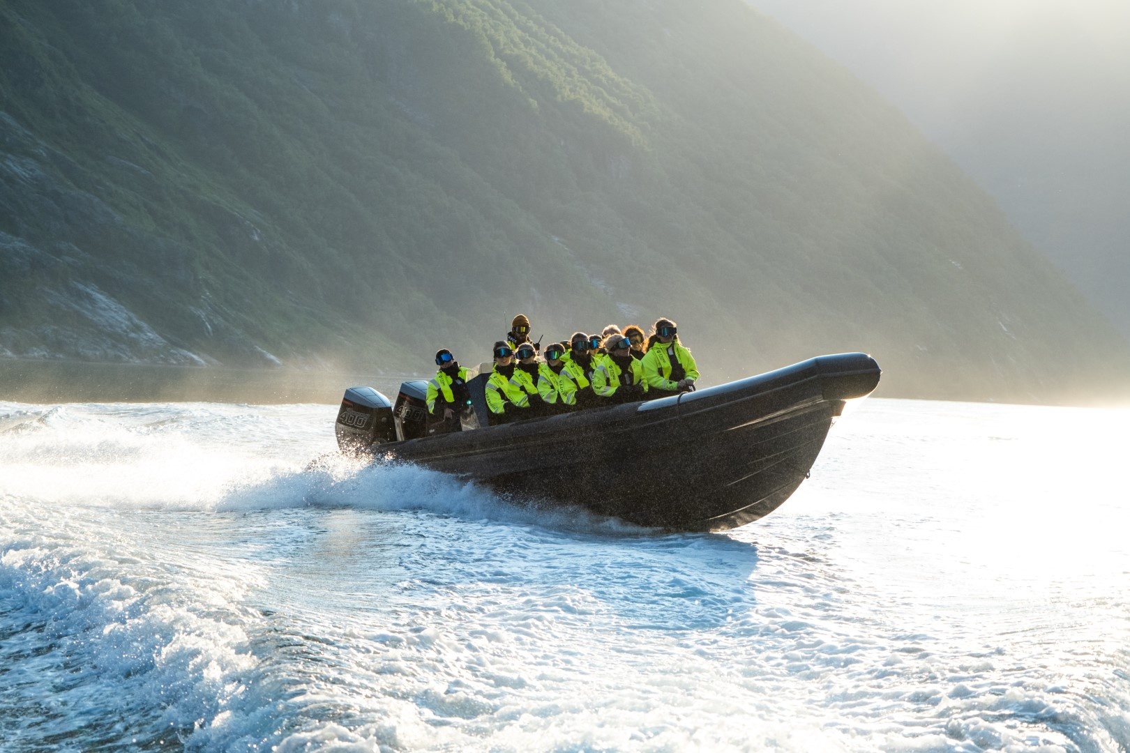 Group in high-visibility jackets on a motorboat in a sunlit fjord.