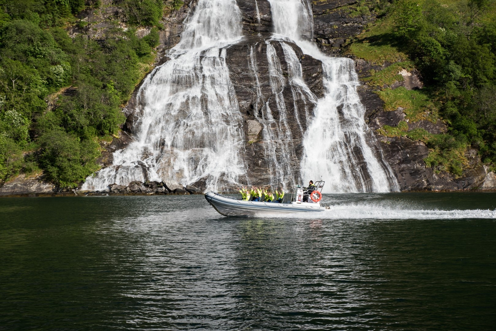 Boat on water near a large waterfall in a lush green landscape.