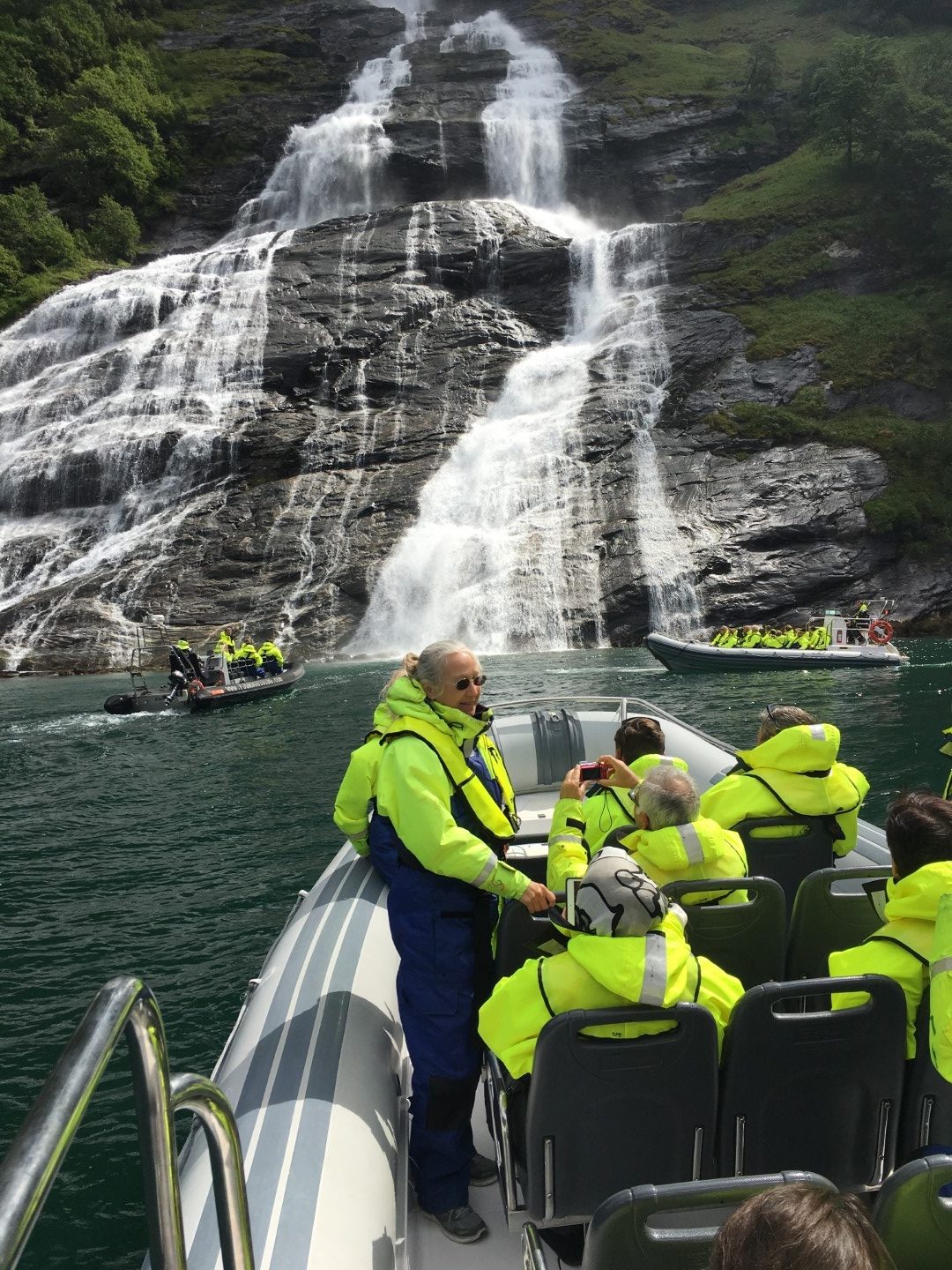 Tourists in life jackets on a boat near a waterfall.