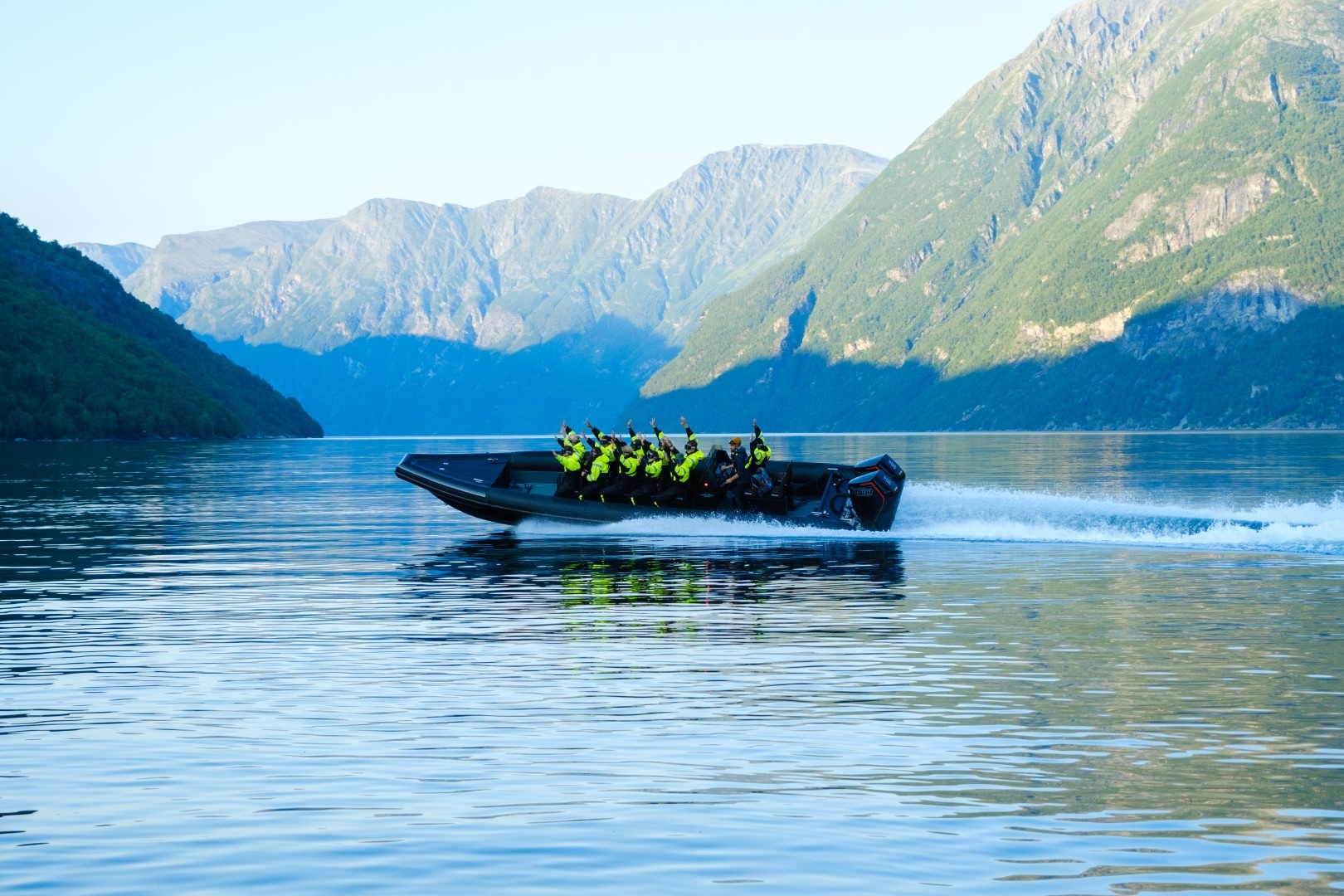 Boat with passengers on a calm lake, surrounded by mountains.