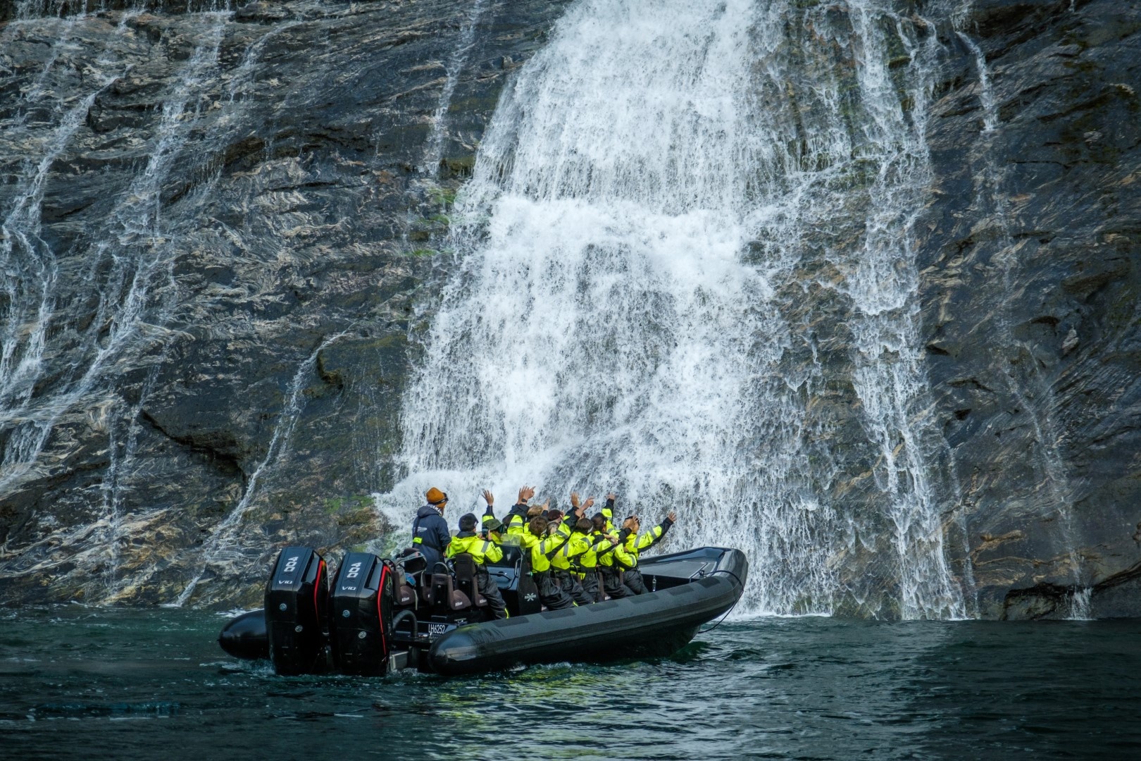 Group in yellow jackets on a boat near a large waterfall.
