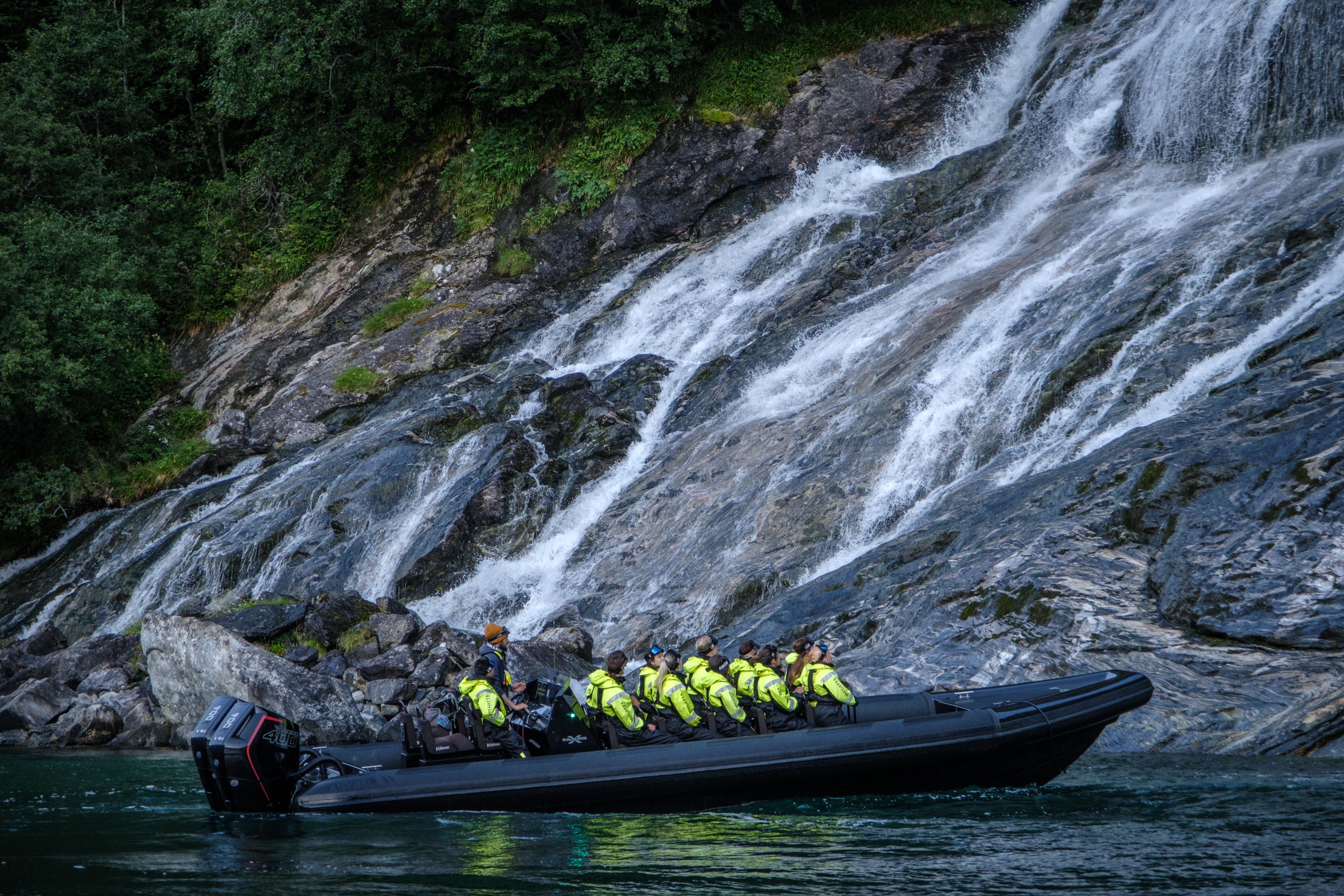 Group in yellow jackets on a boat near a rocky waterfall.
