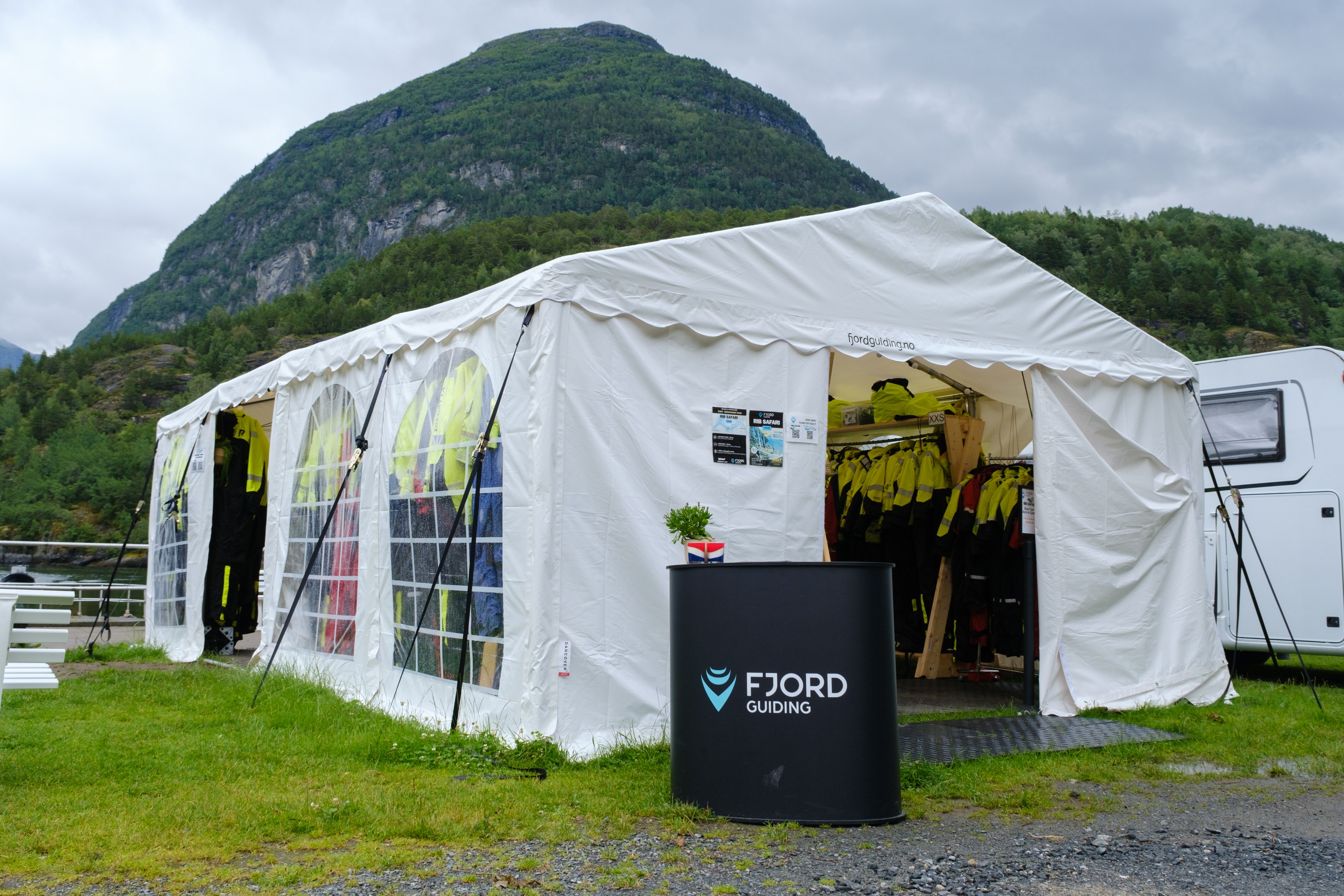 White tent with gear for sale, mountain in background on a cloudy day.