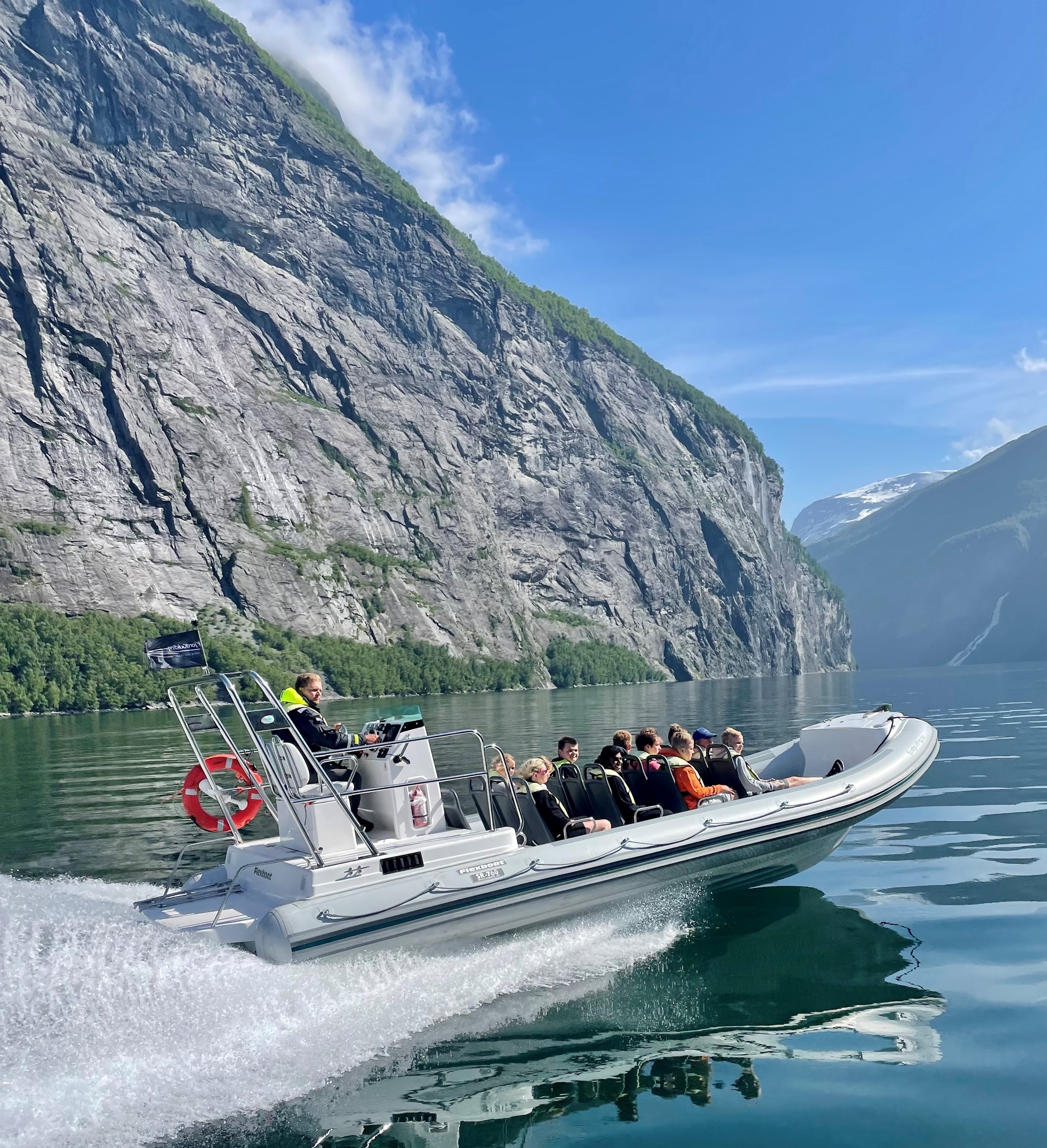 A boat speeds through a fjord with cliffs and clear blue skies.