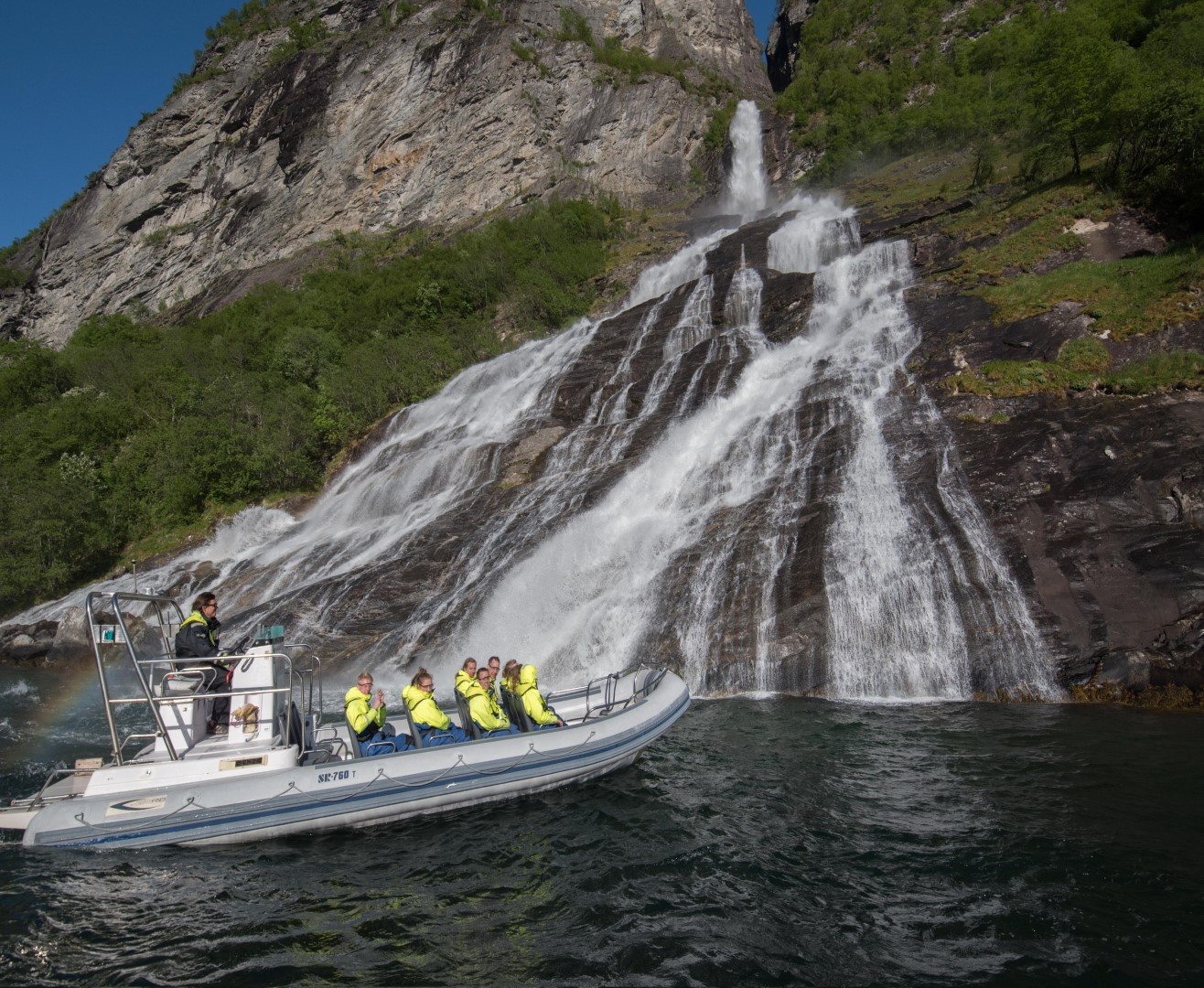 Boat with passengers near a cascading waterfall against rocky cliffs.