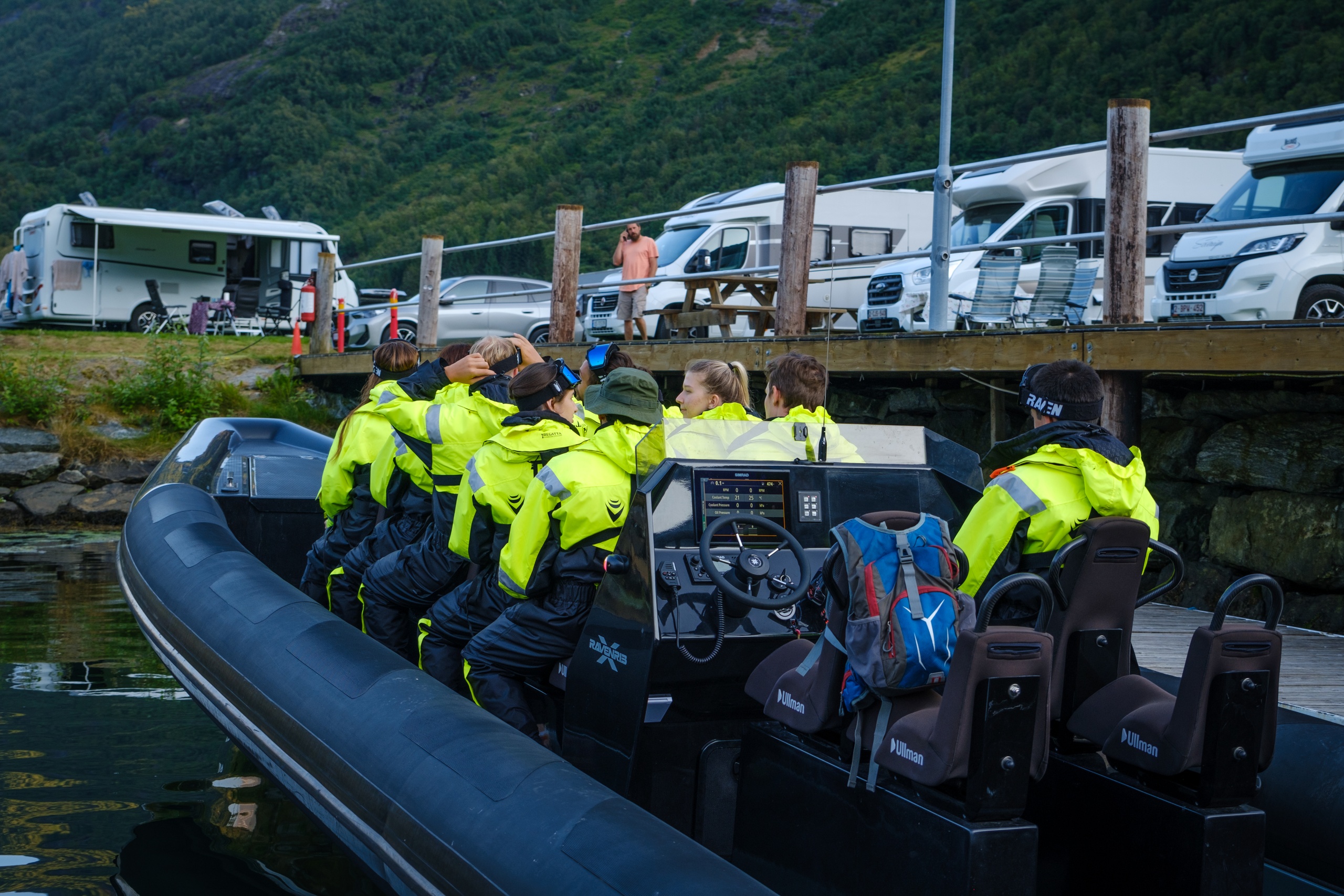 Group in yellow suits seated in a black boat near parked RVs.