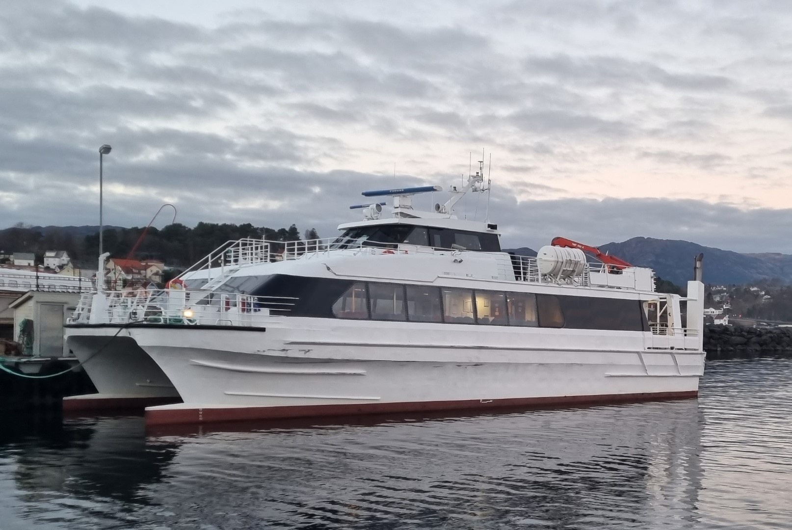 White and blue catamaran ferry docked at a harbor on a cloudy day.