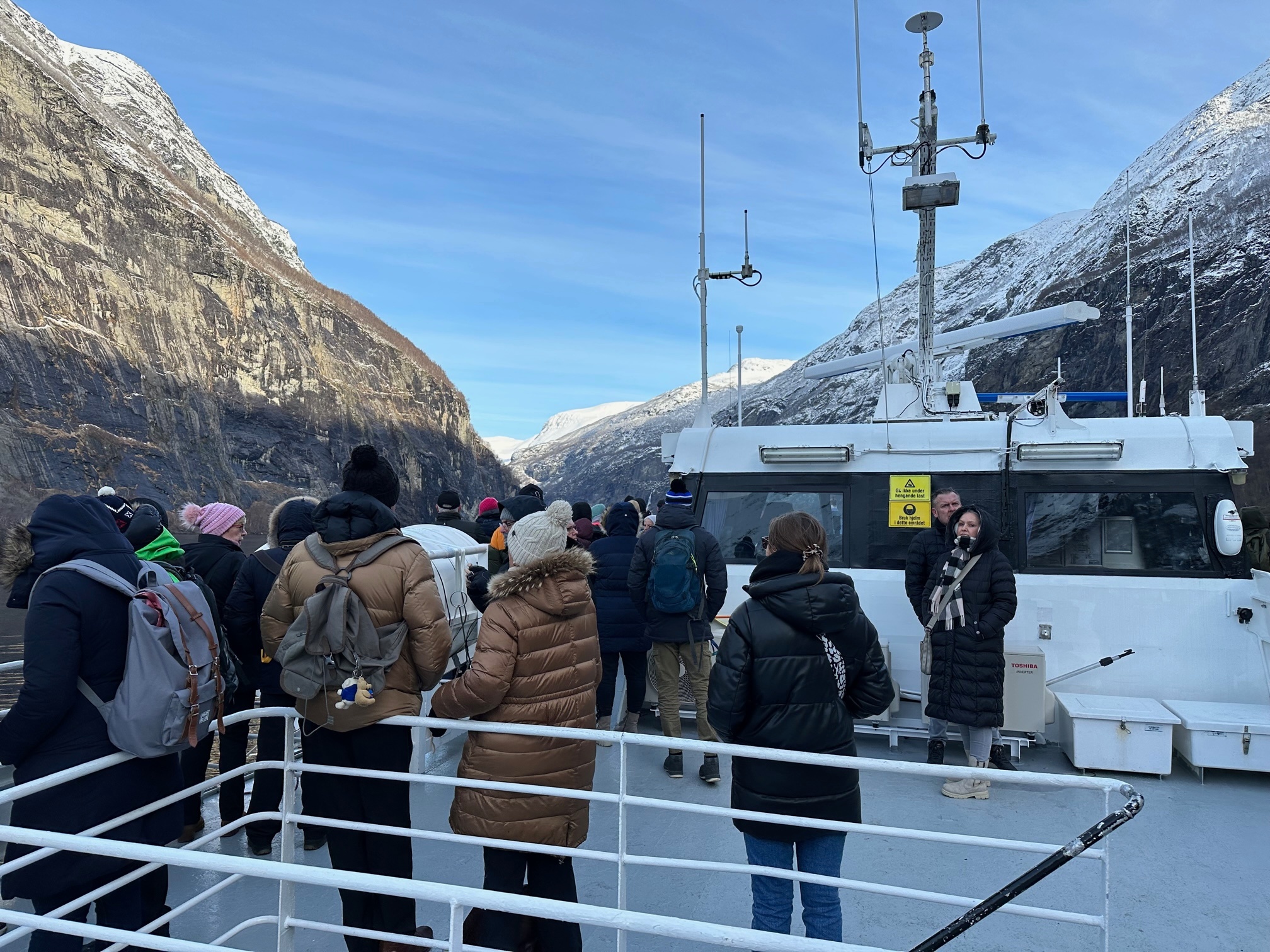 People in winter clothing on a boat surrounded by snowy mountains.