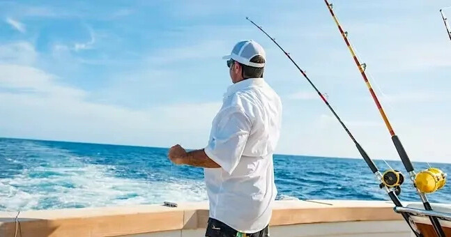 Man on a boat fishing in the ocean with two fishing rods.