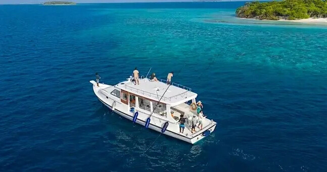 Boat on clear blue water near a small island with green vegetation.